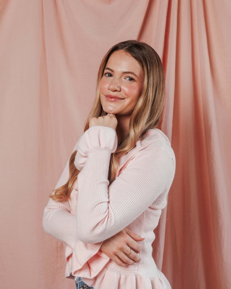Elle smiling, sitting in front of a pink backdrop